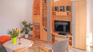 Un ambiente compatto con una TV, mobili in legno, un tavolino con un vaso di fiori e una pianta in vaso.