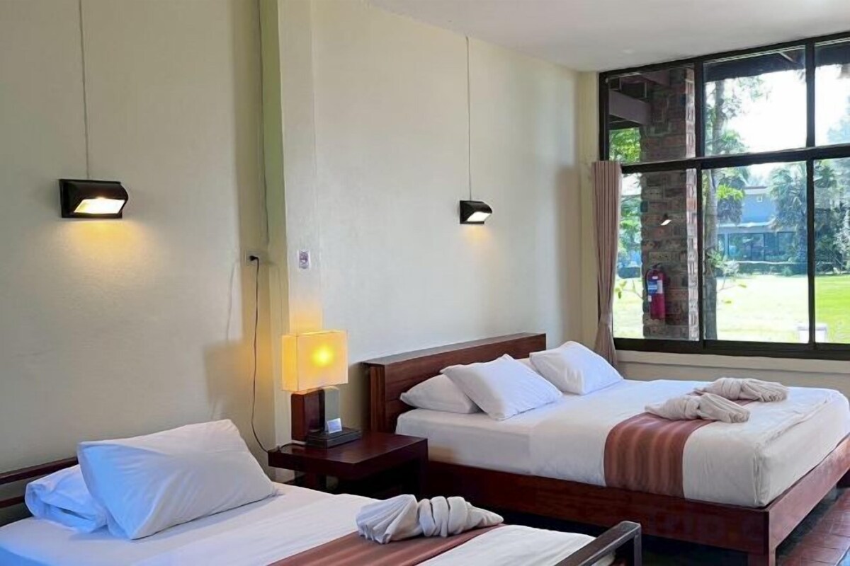 A hotel room with two beds, a window with a view of the outdoors, and a lamp on the nightstand.