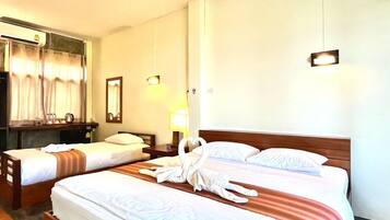 A hotel room with two single beds, a wooden headboard, a desk with a chair, a mirror, and a wall-mounted air conditioning unit.