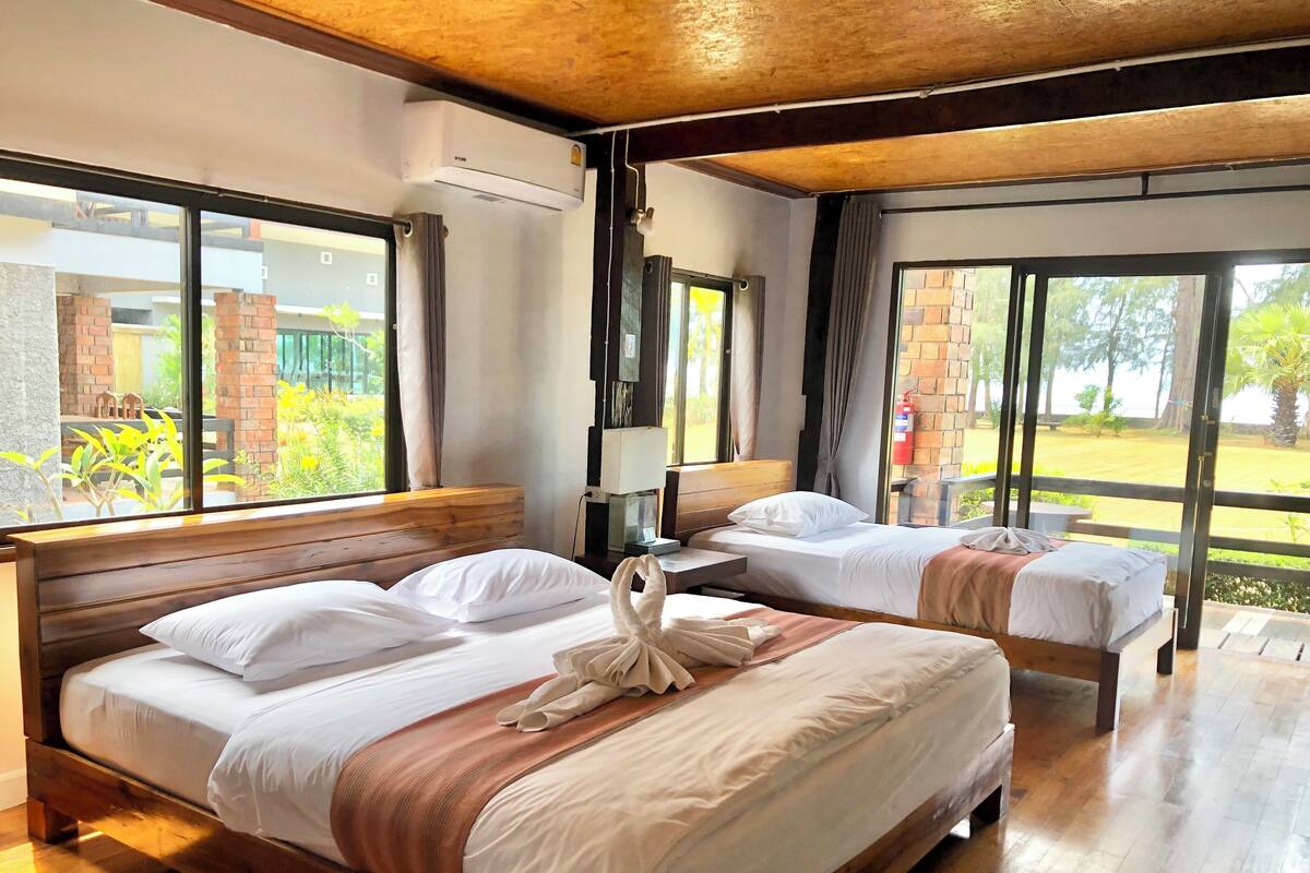 A hotel room with two beds, large windows, a wooden ceiling, and a view of the outdoors.