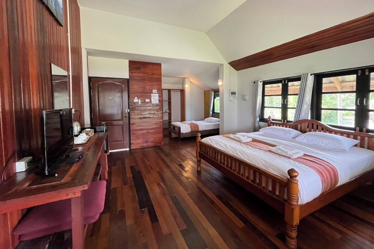 A hotel room with a wooden floor, a bed with white linens, a desk with a computer, and a window with curtains.