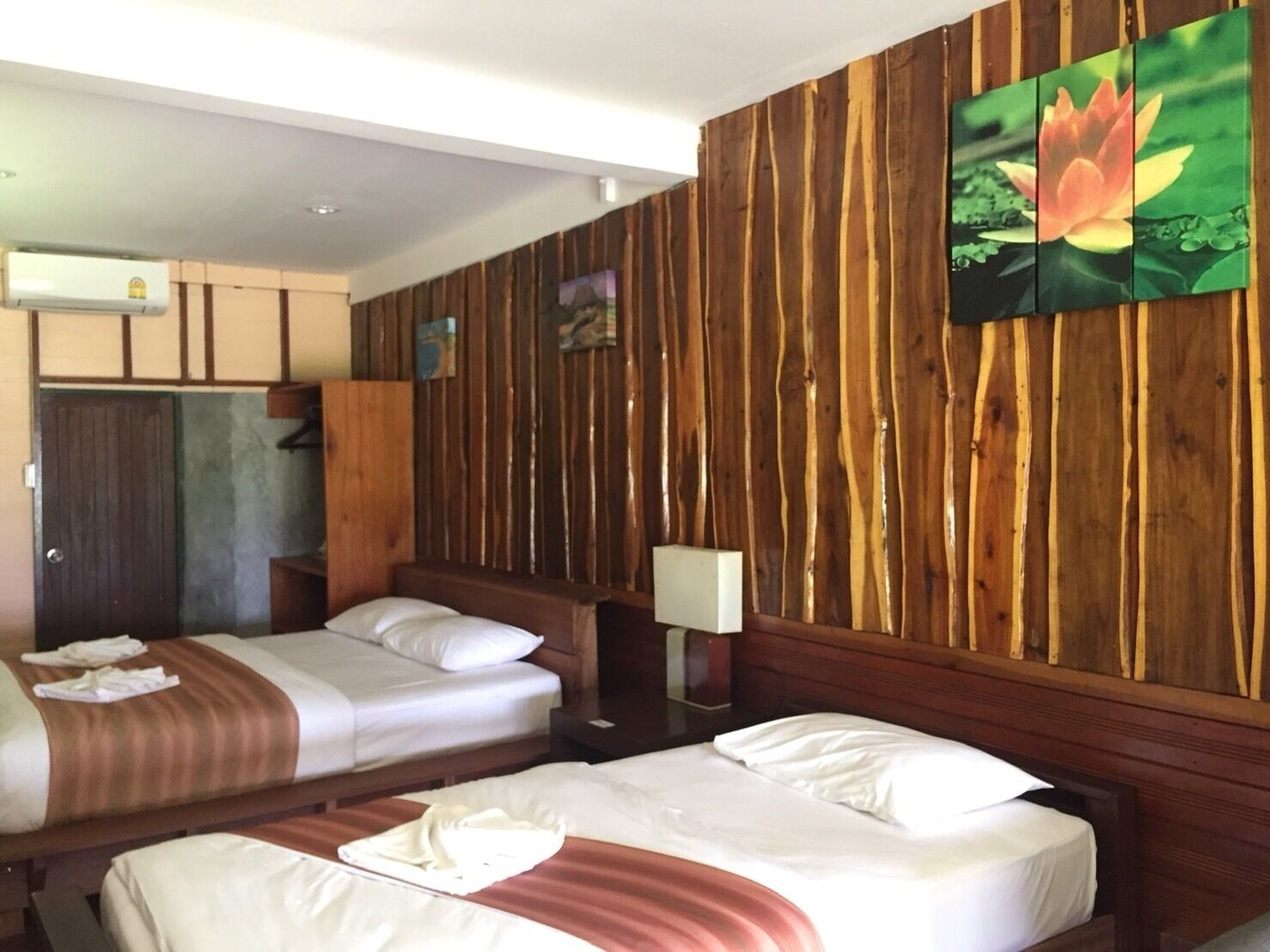 A hotel room with two beds, wooden paneling on the walls, a painting of a lotus flower, and a wardrobe.