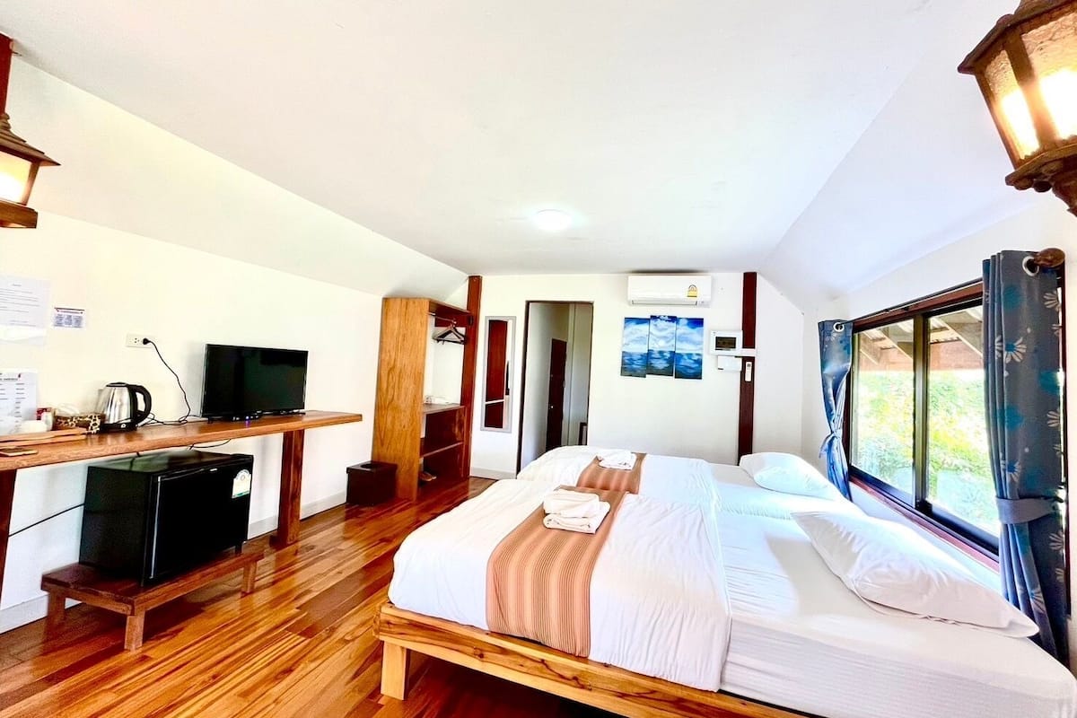 A hotel room with a bed, a desk with a television, a coffee maker, and a window with curtains.