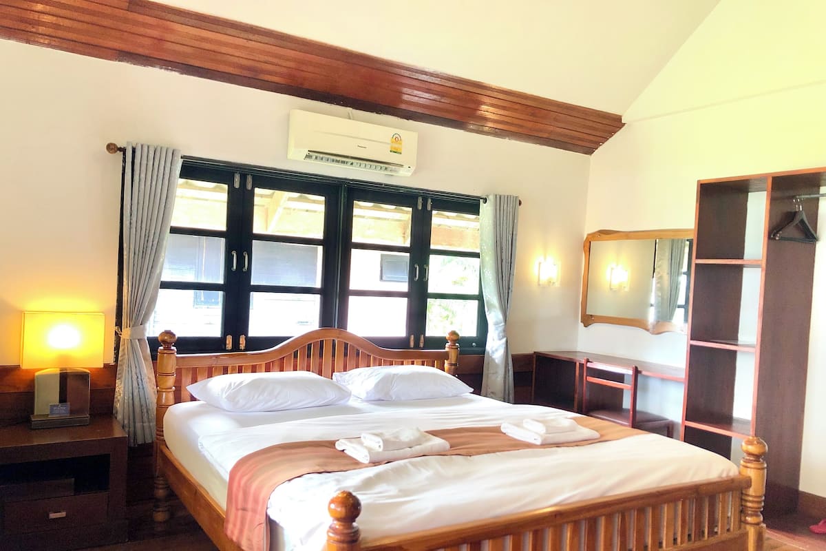 A neatly made bed with white linens, a wooden headboard, and a window with curtains.