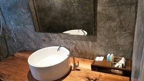 Bathroom features a large, round sink and a mirror above, with a small shelf for toiletries.