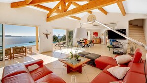 A spacious living room with a red sofa, a coffee table, and a view of the ocean. - Somptueuse Villa l'Oasis avec vue mer By HC (Carqueiranne)