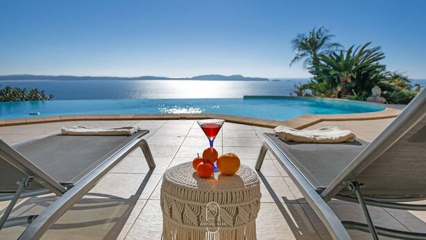 A poolside view with lounge chairs, a round table with fruits and a martini glass, and a clear view of the sea and distant islands. - Somptueuse Villa l'Oasis avec vue mer By HC (Carqueiranne)