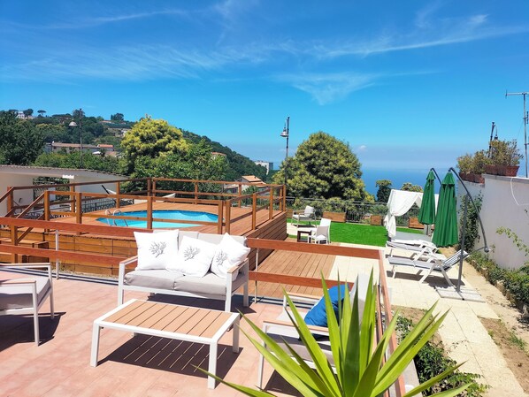Area piscina sul tetto con pavimento in legno, poltrone relax e vista sul mare.
