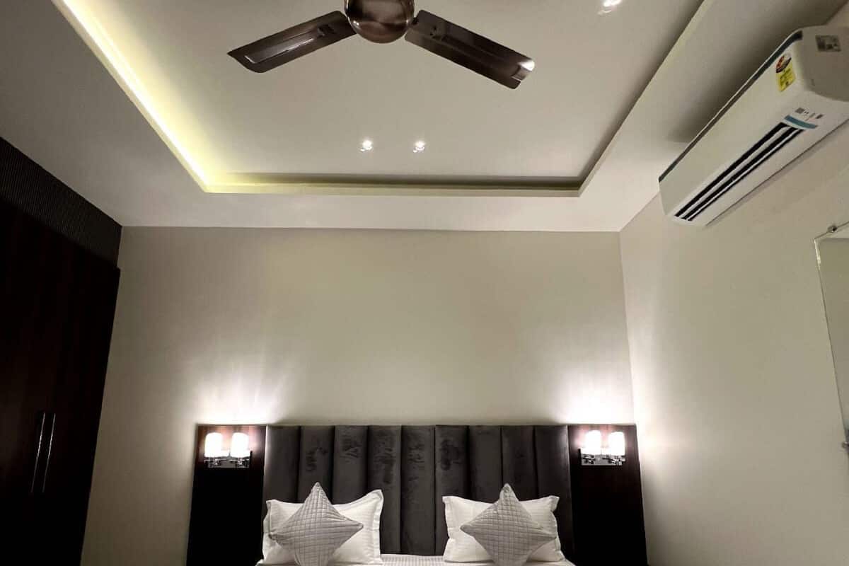 A modern hotel room with a large bed, a ceiling fan, recessed lighting, and an air conditioning unit.