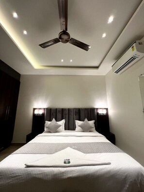 A modern hotel room with a large bed, a ceiling fan, recessed lighting, and an air conditioning unit.