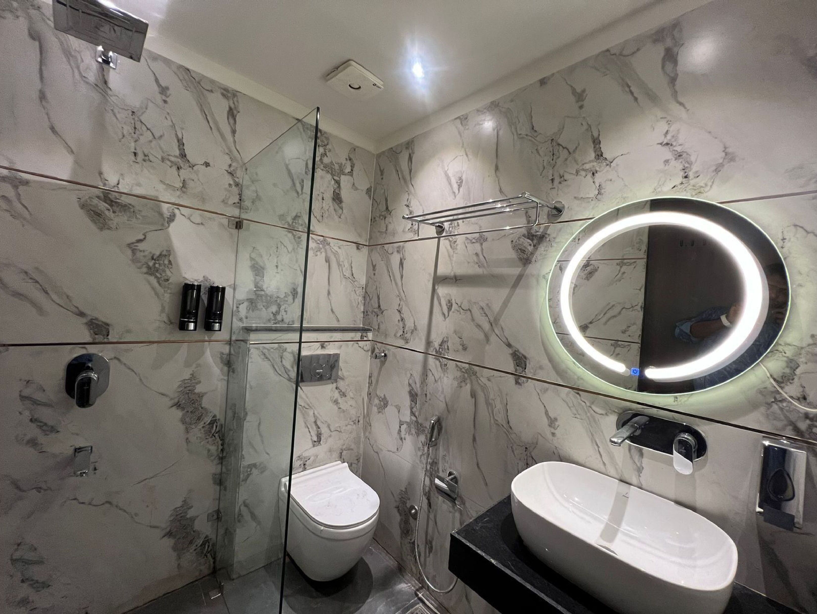 A bathroom with marble walls, a toilet, a sink with a mirror, and a shower area.