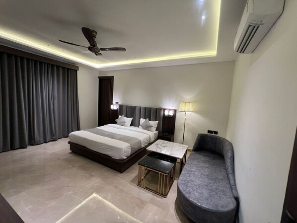 A modern hotel room with a large bed, a desk, a chair, and a ceiling fan. - Hotel Majestic Grand By MNG Rooms (Kanpur)