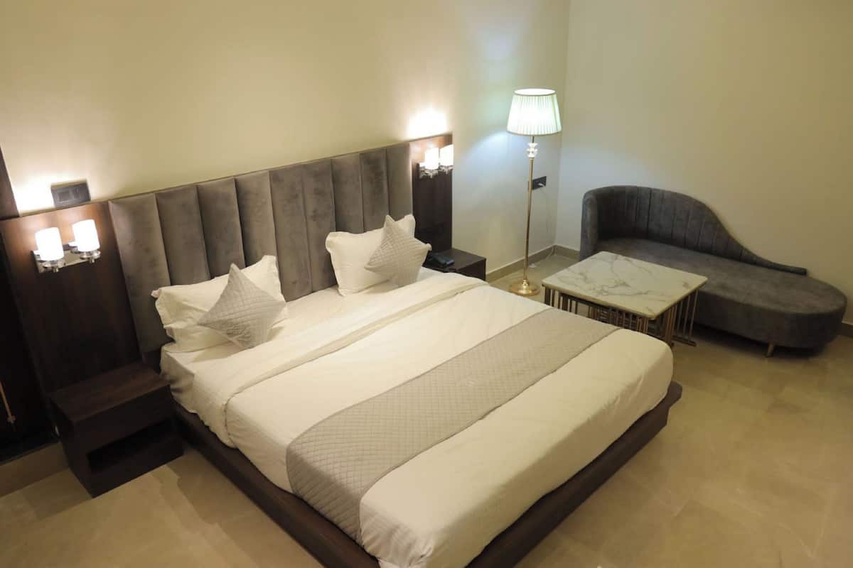 A hotel room with a large bed, bedside tables, a nightstand, a lamp, and a curved armchair.