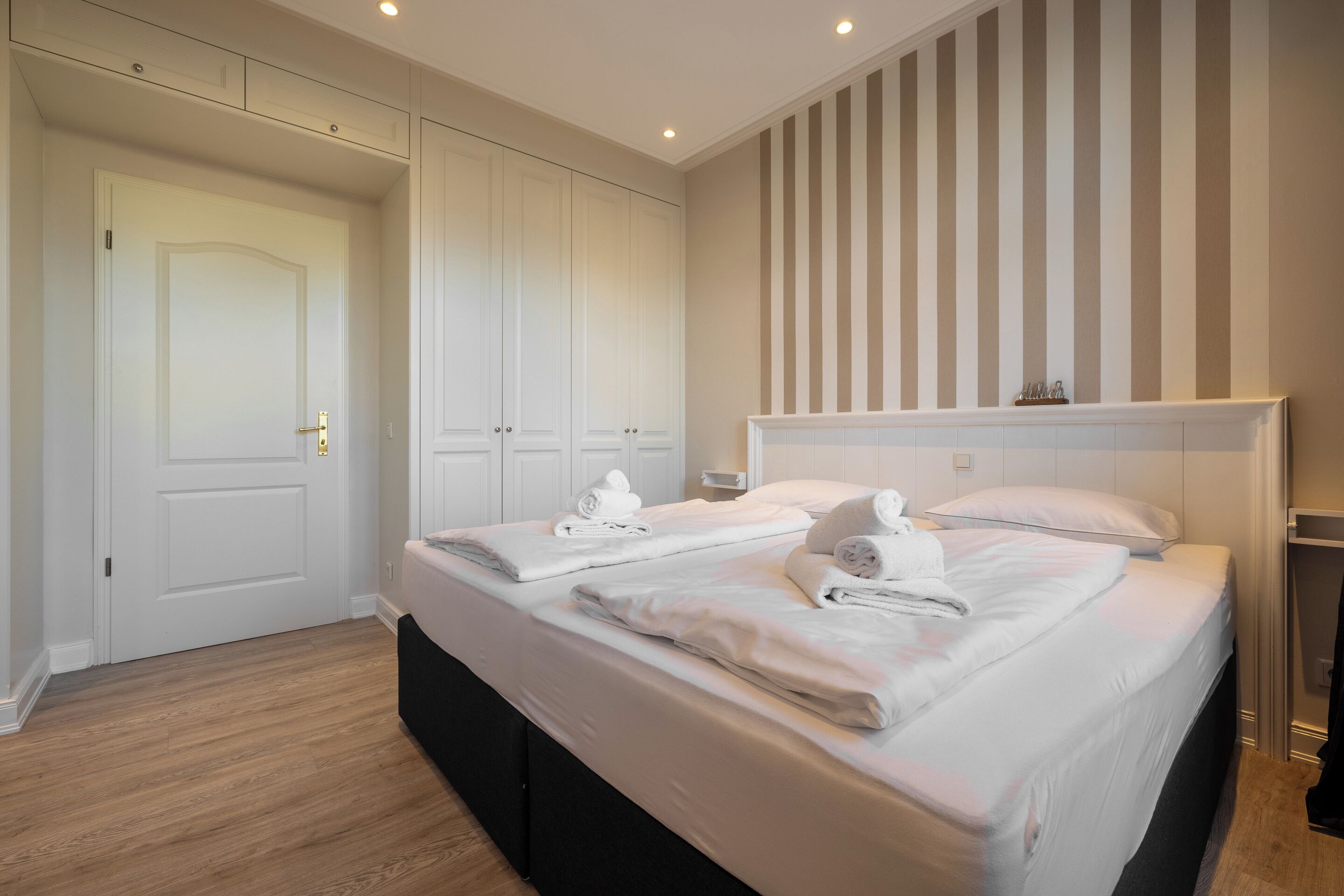 A hotel room with a large bed, a wardrobe, and a striped wall.