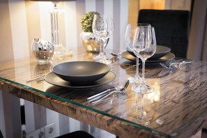 Une table à manger avec un plateau en verre, entourée d’assiettes, de bols et de verres à vin.