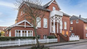 Et rødt murstenshus med hvid gelænder og en balkon, samt en trappe til indgangen.