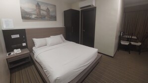 Een hotelkamer met een bed, een nachtkastje met een telefoon, een schilderij van een brug, een kledingkast en een kleine tafel met stoelen.