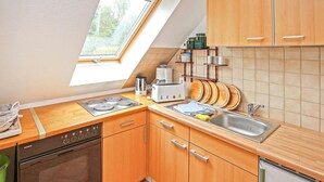 Eine Küche mit Holzausstattung, einem eingebauten Ofen, einer Spülmaschine, einem Spülbecken und einem Fenster mit Blick auf Grünflächen.