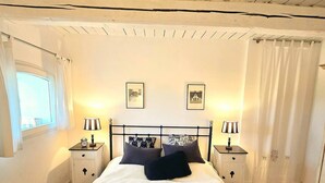 Un dormitorio con cama, dos mesitas de noche con lámparas, una ventana con cortinas y un techo con vigas de madera.