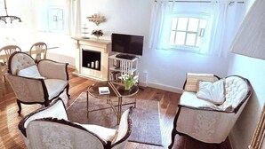 Un salón con piso de madera, chimenea, televisor y varias sillas tapizadas.