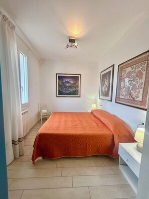 A bedroom with a bed, a chair, a nightstand, and two framed pictures on the wall. - Garden Retreat by the sea on Albarella (Rosolina)