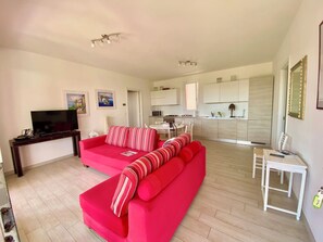 A modern living room with a red sofa, a TV, and a dining area with a white table and chairs. - Garden Retreat by the sea on Albarella (Rosolina)