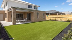 Une maison moderne à deux étages, dotée d’un patio et d’une pelouse bien entretenue.