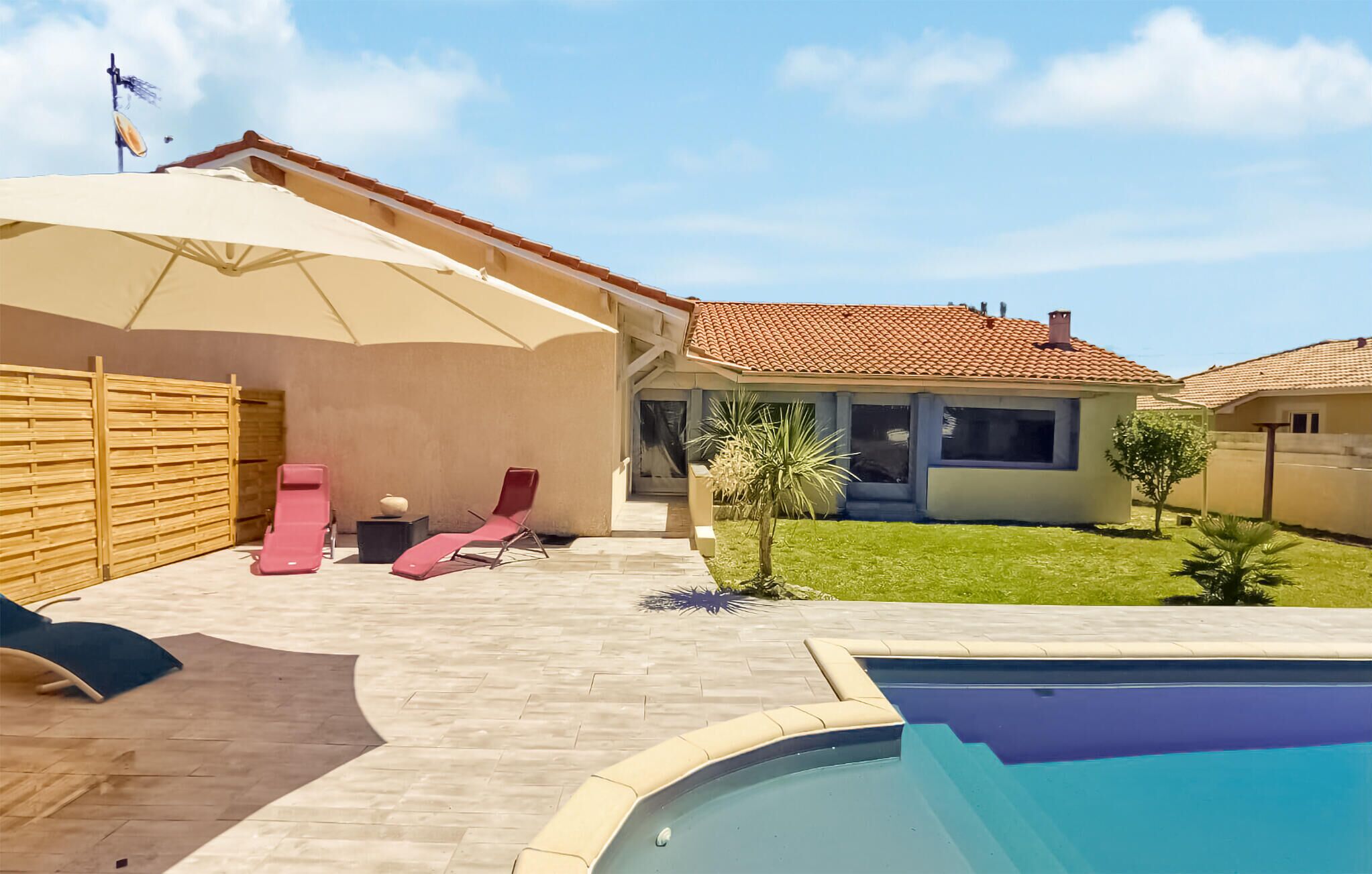 Un pati darrere amb una piscina, una zona de porxo coberta i una casa amb teulada d'rajola.