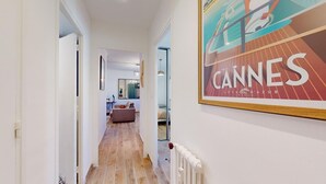 Un corridoio con pavimento in legno che conduce a una zona giorno con divano e tavolo da pranzo. Sul muro, un quadro con l'immagine del Festival di Cannes.
