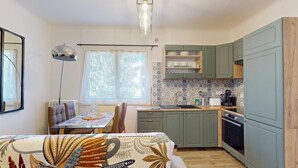 Una cucina compatta con mobili verdi, un'area pranzo con tavolo e sedie, e una finestra che permette l'ingresso di luce naturale.