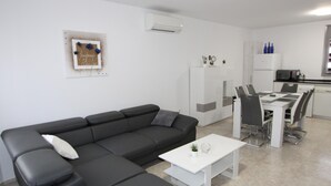 A modern living room with a black sectional sofa, a white coffee table, and a dining area with a white table and chairs. - Beachside Oasis: Private Pool, Optional A/C, Free Wi-Fi, Pet Friendly, Near Dog Beach (Deltebre)