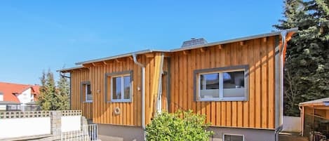 Ein Holzhaus mit zwei Fenstern, einem kleinen Garten und einem gepflasterten Weg.