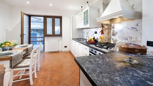 Cozinha moderna com armários brancos, bancada de mármore e vista através de uma porta de vidro.