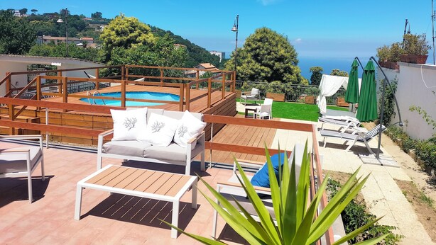 Uma área de piscina no terraço com deck de madeira, espreguiçadeiras e vista para o mar.