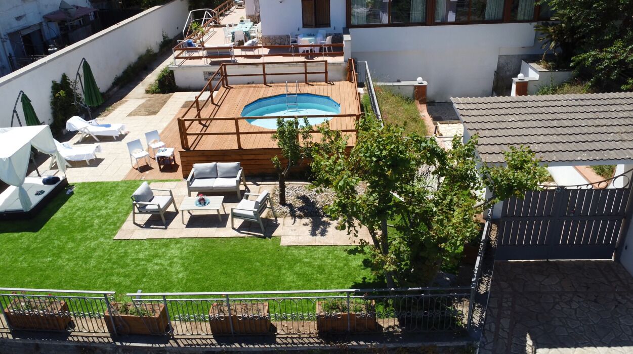 A rooftop pool area with a wooden deck, lounge chairs, and a small grassy area.