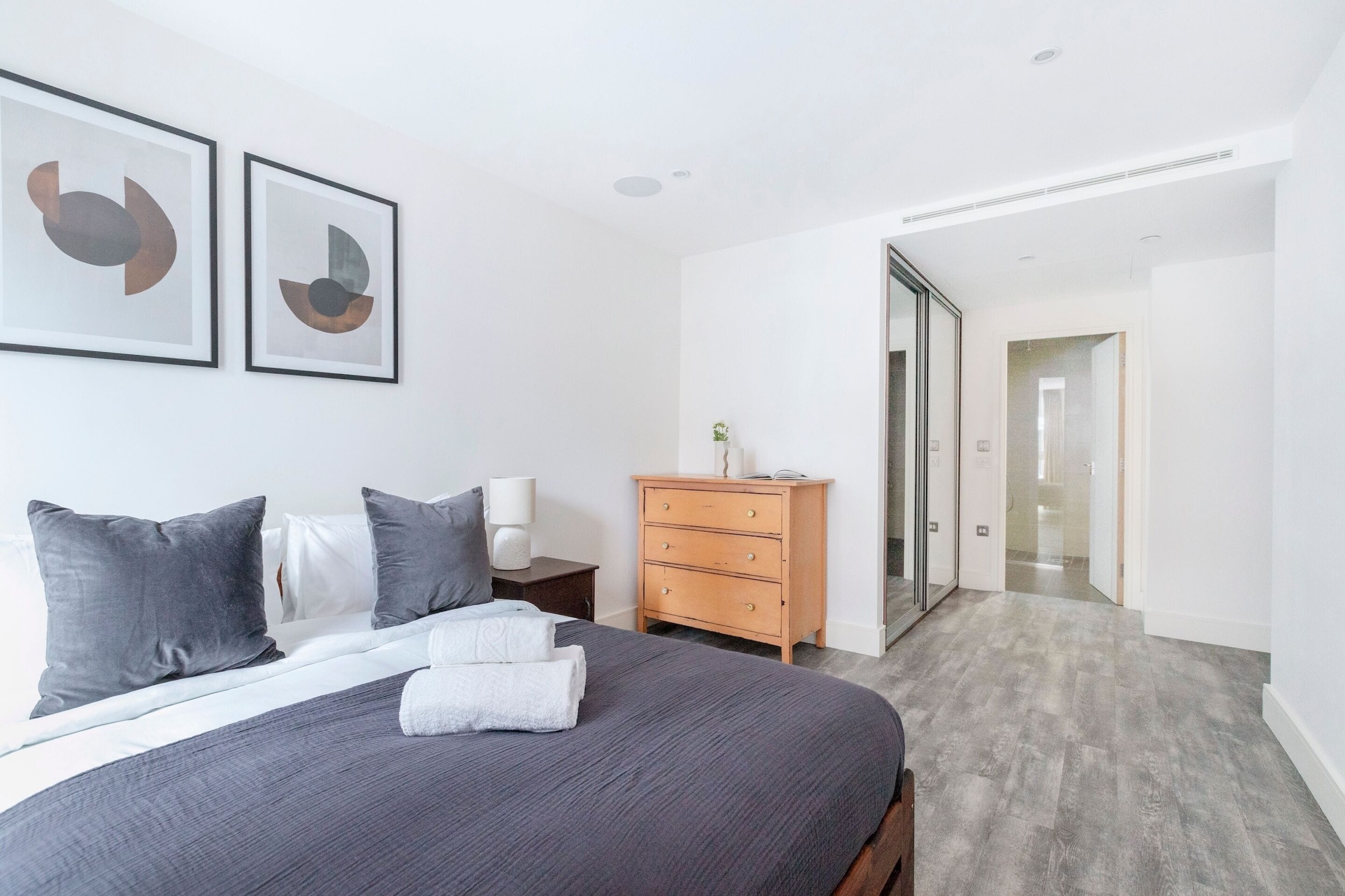 A modern bedroom with a large bed, a wooden dresser, and a glass door leading to another room.