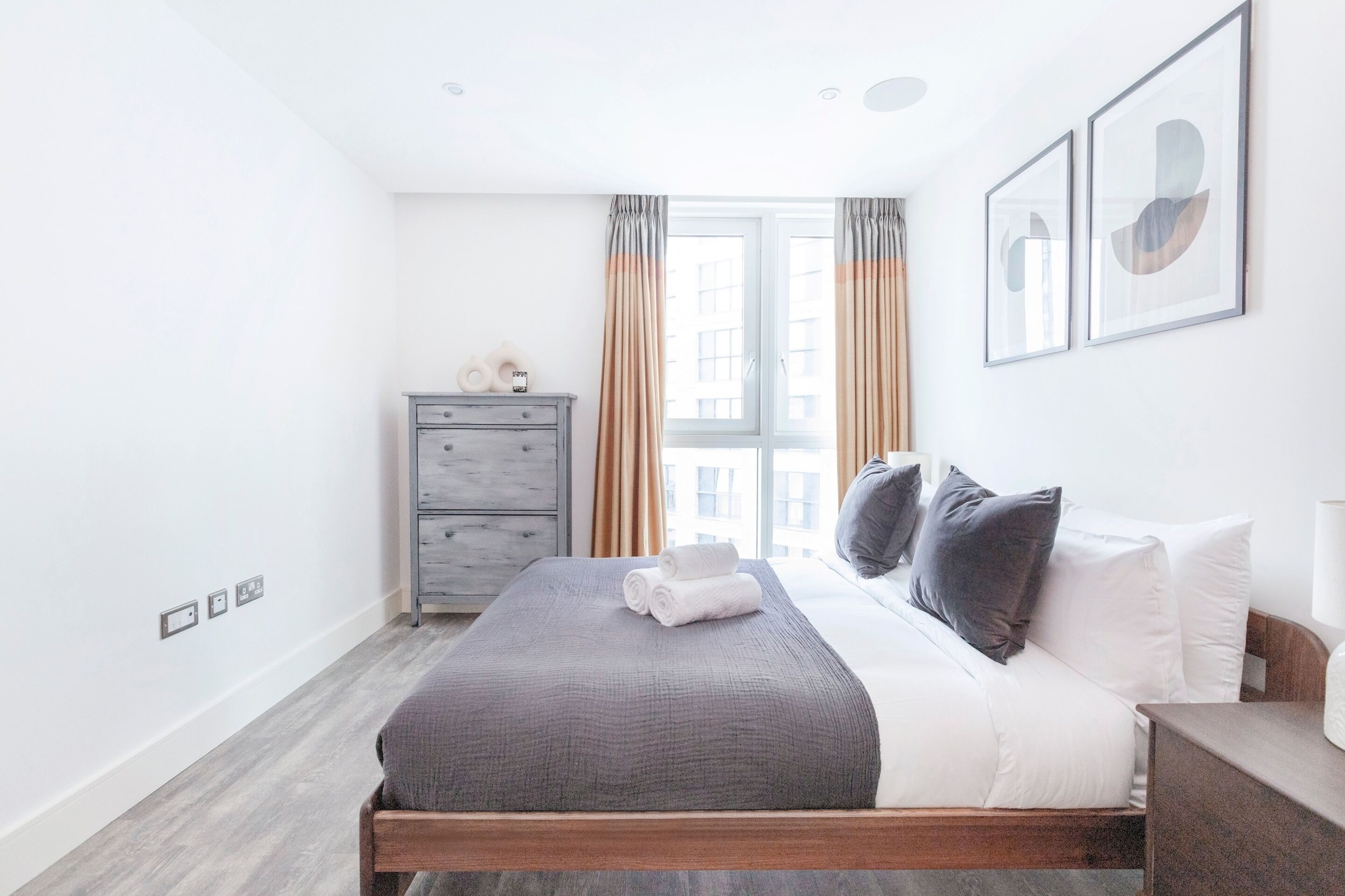 A modern bedroom with a bed, a dresser, and a window with curtains.
