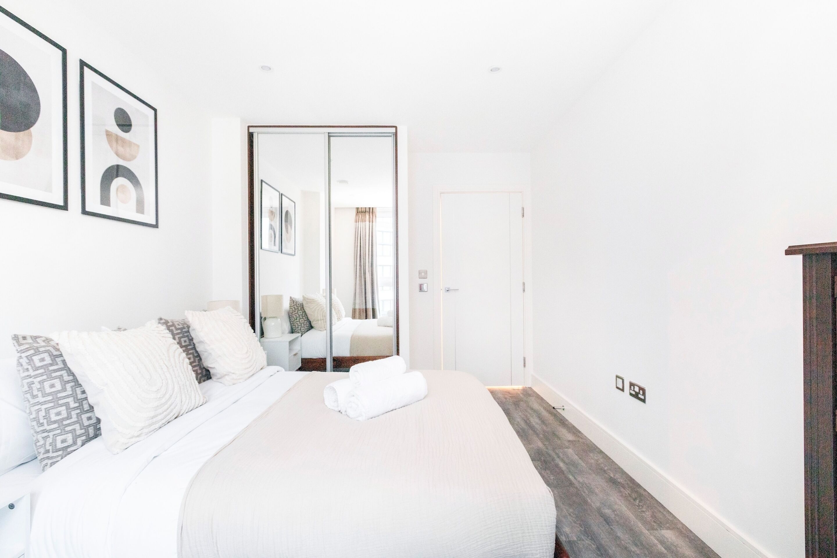 A modern hotel room with a large bed, a wardrobe, and a mirror.