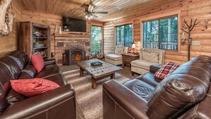 L’intérieur d’un chalet confortable, avec une cheminée, des canapés en cuir, un téléviseur et de grandes fenêtres.