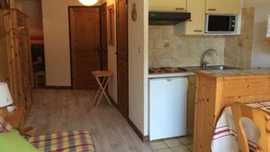 A compact kitchen with wooden cabinets, a microwave, a small refrigerator, and a dining area with a table and chairs. - 2-room apartment for 5 people, Châtel, balcony, near center (Châtel)