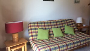 A plaid sofa with green cushions, a wooden side table with a red lamp, and a small wooden stool. - 2-room apartment for 5 people, Châtel, balcony, near center (Châtel)