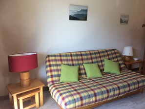 Een gestreepte bank met groene kussens, een houten bijzettafeltje met een rode lamp en een klein houten krukje.