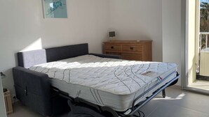 A bedroom with a bed, a dresser, and an air conditioning unit. - Renovated Studio with Balcony, A/C, Wi-Fi and Modern Amenities - 5 Min Walk to Thermes (Balaruc-les-Bains)