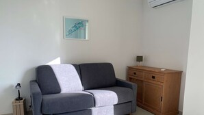 A modern living room with a grey sofa, a wooden cabinet, and a framed map on the wall. - Renovated Studio with Balcony, A/C, Wi-Fi and Modern Amenities - 5 Min Walk to Thermes (Balaruc-les-Bains)