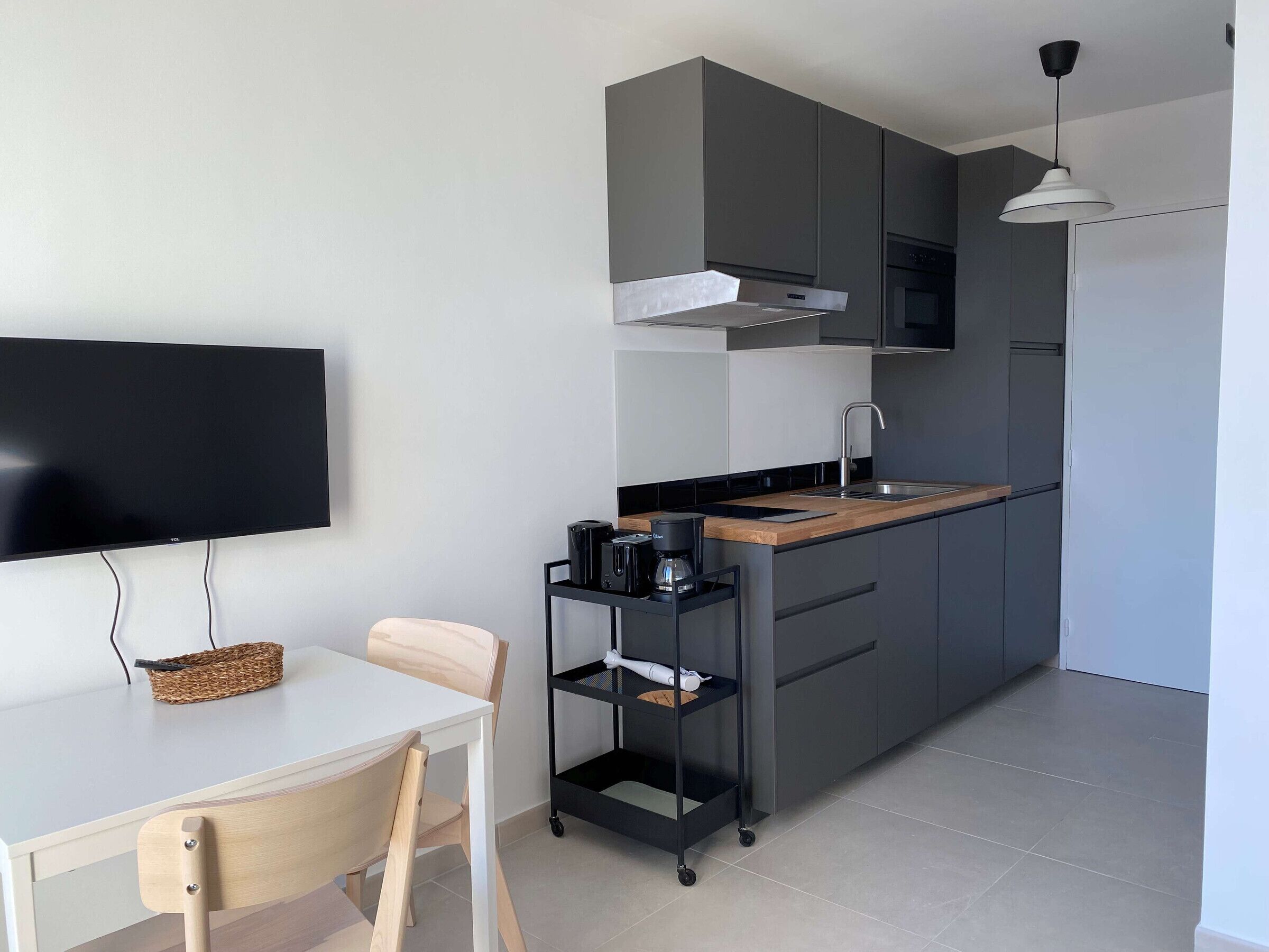 A modern kitchen with grey cabinets, a wooden countertop, a built-in oven, and a black coffee machine.
