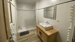 Un baño moderno con cabina de ducha de vidrio, tocador de madera con lavamanos y un espejo sobre el tocador.