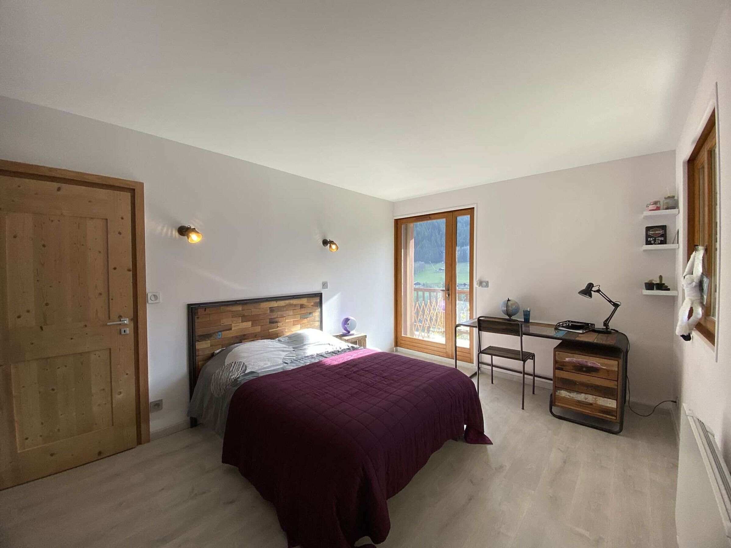 A bedroom with a bed, a desk, a chair, a window, and a door.