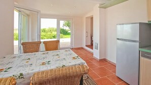 Cozinha compacta com geladeira, mesa de jantar com cadeiras e uma porta de vidro corrediça que dá para uma área externa.