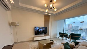A modern living room with a flat-screen TV, a sofa set, a coffee table, and a view of a cityscape through large windows. - Luxury Flat Stunning Nile View (Giza)