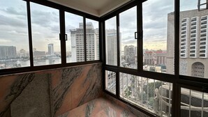 A room with large windows offering a city view, marble flooring, and a modern ceiling light fixture. - Luxury Flat Stunning Nile View (Giza)